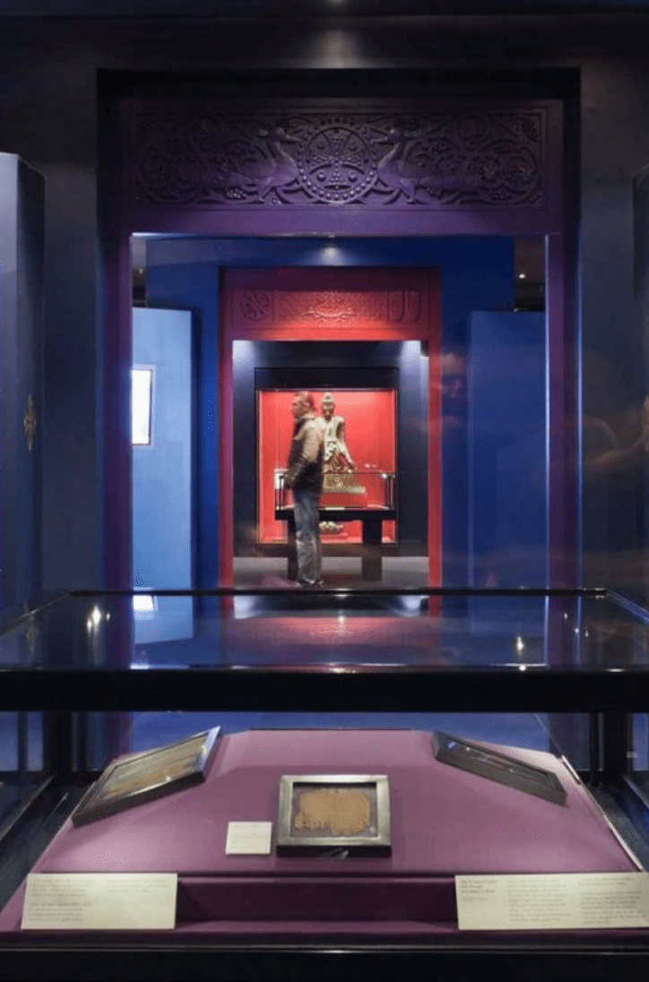 An exhibition case with silver framed books in it. Door in the background, a man is standing at the back.
